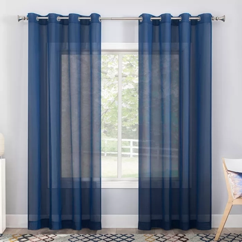 Calypso Sheer Voile Grommet Window Curtains hanging on a window, filtering sunlight