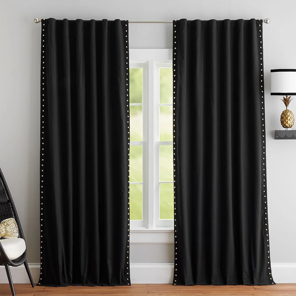 black velvet curtains with a vertical row of gold studs along each side hang on a window